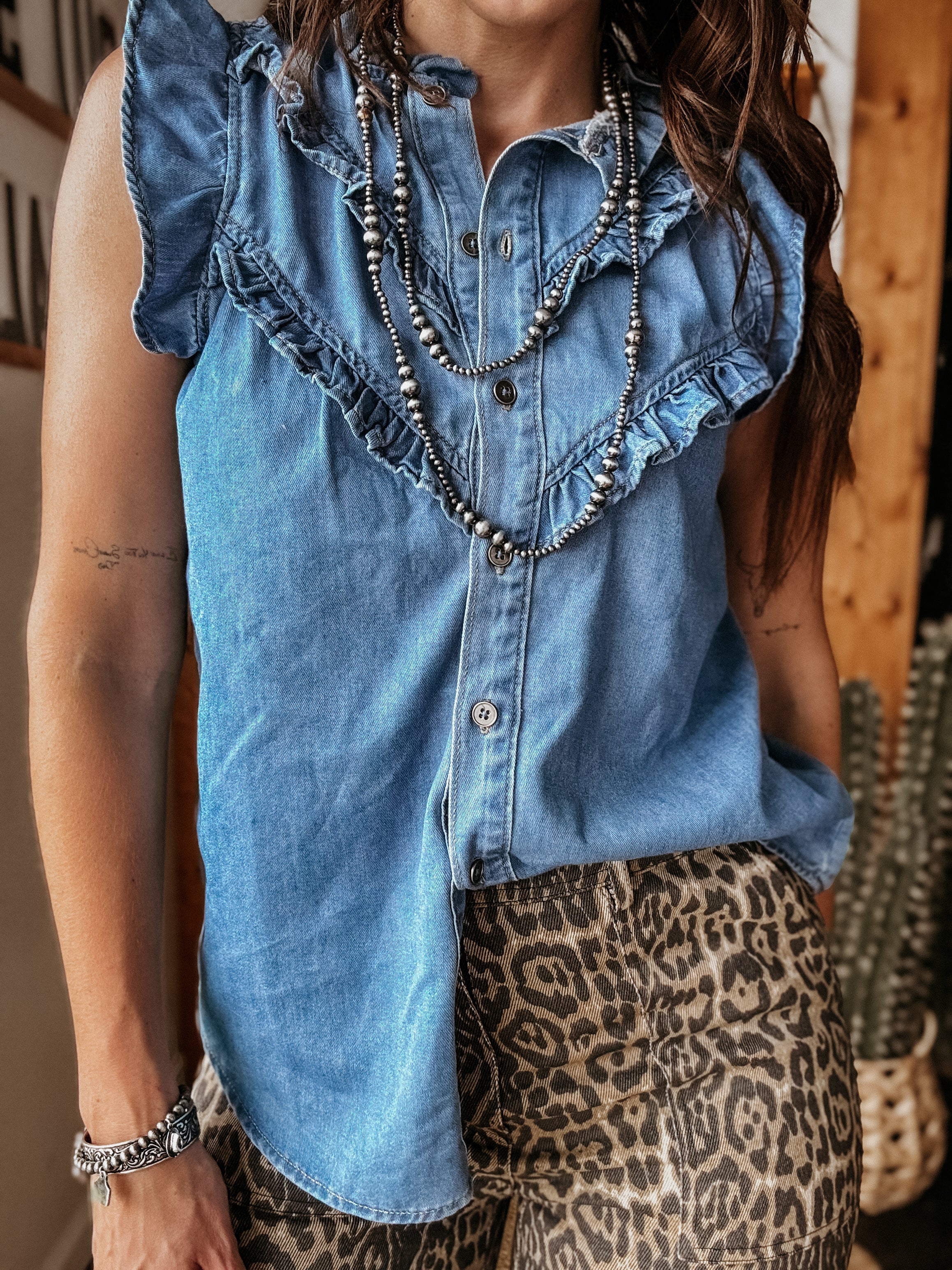Woman in sleeveless ruffle denim top, leopard print pants, and layered western jewelry