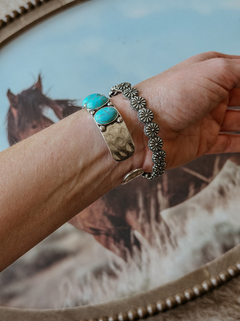 Hand wearing turquoise stone western cuff bracelet and silver floral concho bracelet