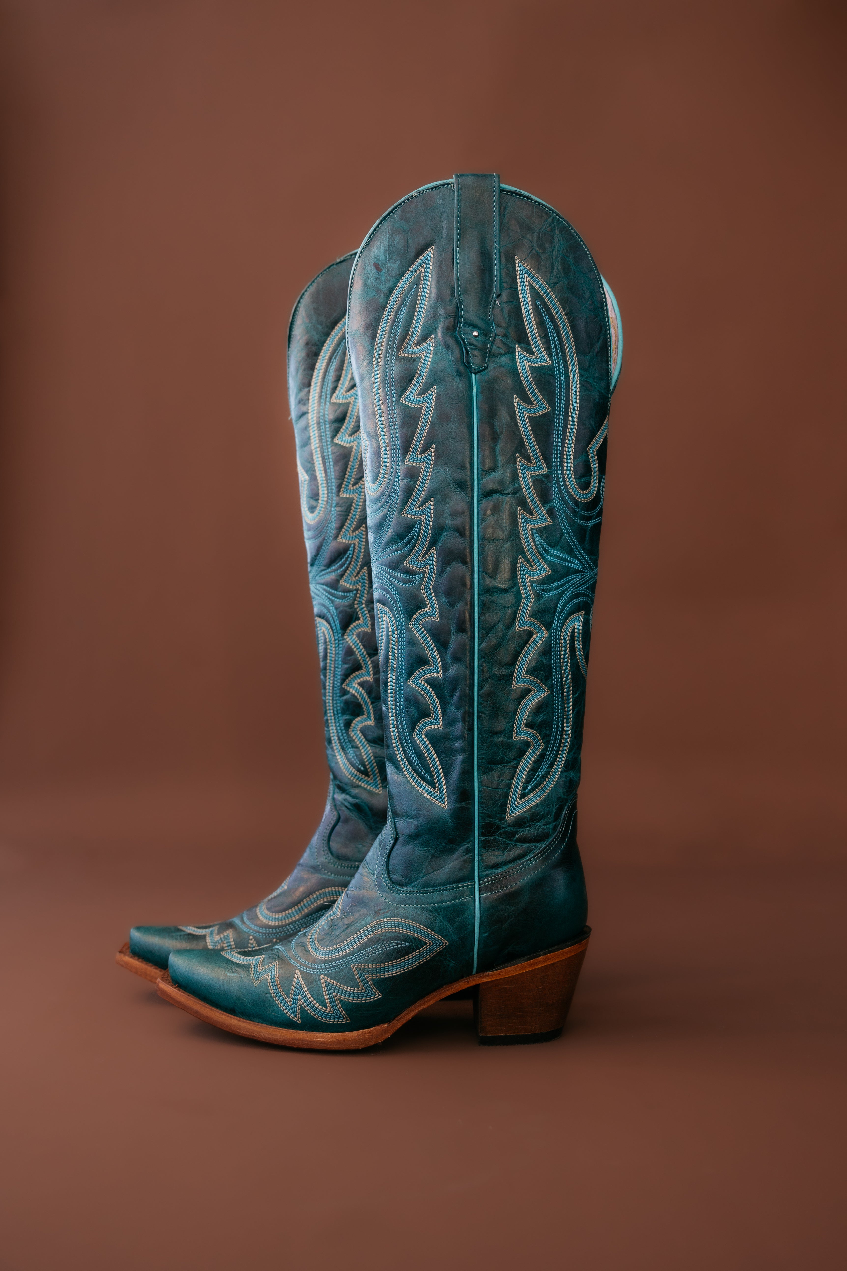 Teal embroidered western cowgirl boots with pointed toes and block heels on brown background