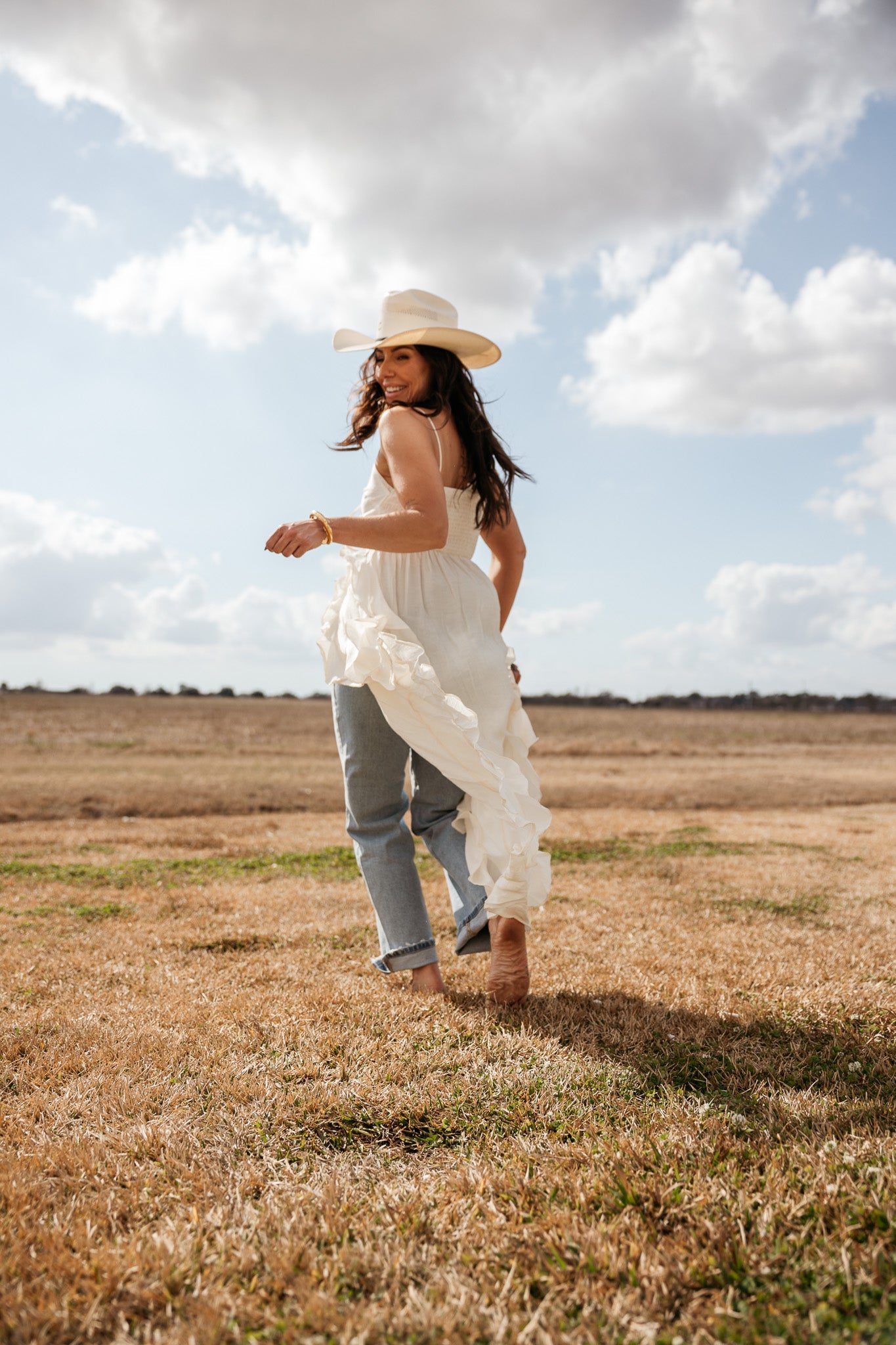 Woman in a white cowboy hat, ruffled boho dress, and jeans in a western field