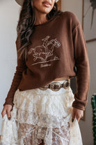 Woman in brown western sweater with horse graphic, lace skirt, and concho belt