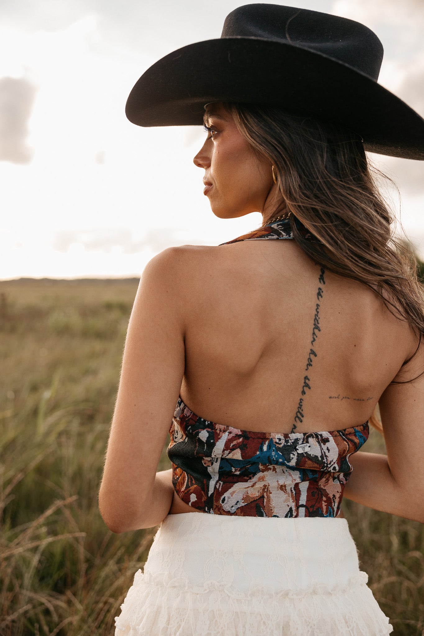 women wearing horse pattern halter top with low back and a white skirt standing in a field. 