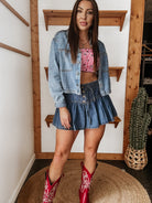 Woman in a denim jacket and skirt, red cowgirl boots, and gingham crop top, western boho style