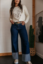 Woman in a cowgirl graphic sweatshirt, wide-leg western jeans, and boho turquoise belt