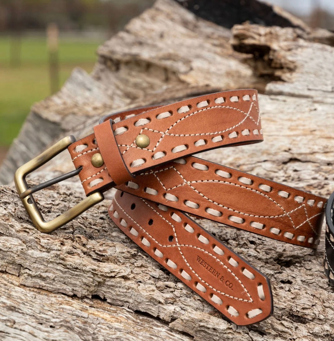Brown tooled leather western belt with brass buckle and white stitching on wood