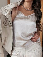 Woman in western boho outfit with fringe skirt, white embroidered jacket, and silver choker