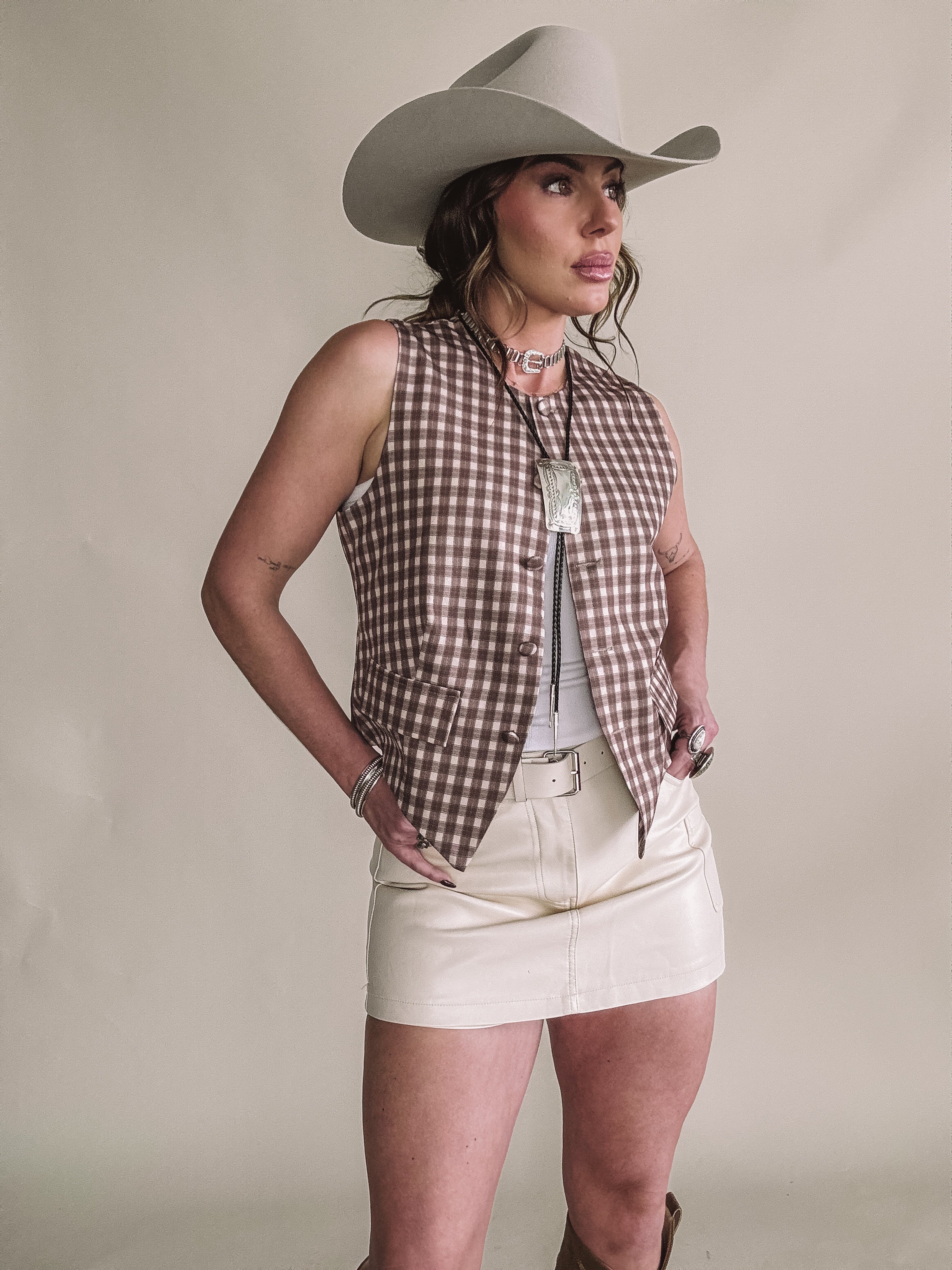 Woman in western outfit with beige cowboy hat, plaid vest, cream mini skirt, and statement necklace.