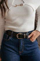 Woman wearing a white ribbed sweater, high-waisted jeans, and a western black belt with gold buckle