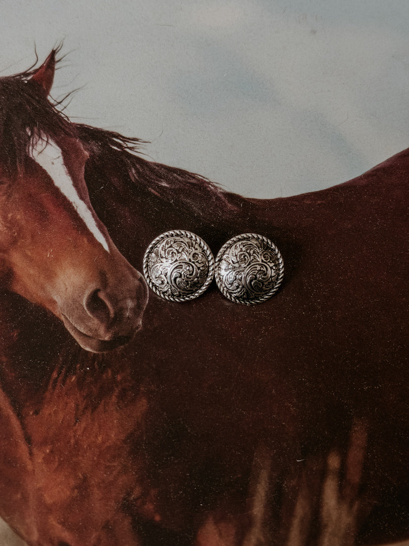 Western silver concho earrings with engraved design, styled on a horse background