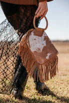 Cow print fringe handbag with braided handle, styled with black lace skirt and western boots
