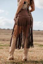 Woman wearing brown fringe western skirt with stud details and cowboy boots outdoors