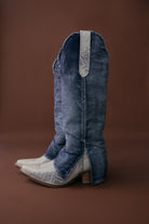 Denim western cowgirl boots with pointed toe and faux snakeskin detail on brown background