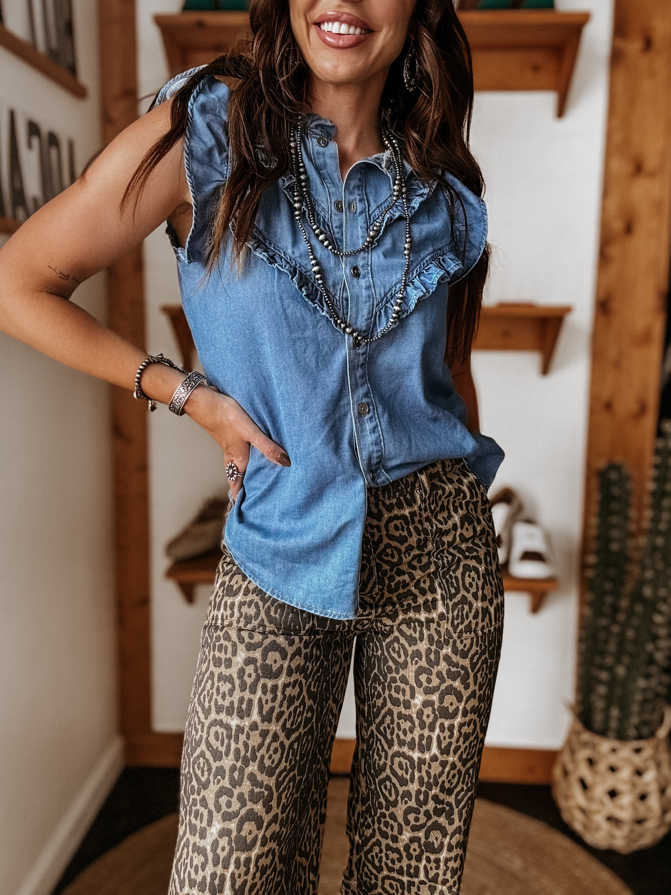 Woman wearing sleeveless denim ruffle top with leopard print wide-leg pants, western jewelry