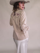 Woman in cream western embroidered shirt, satin skirt, and cowboy hat, western boho style