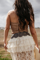 Woman in boho western lace skirt, leather corset top, and concho belt outdoors