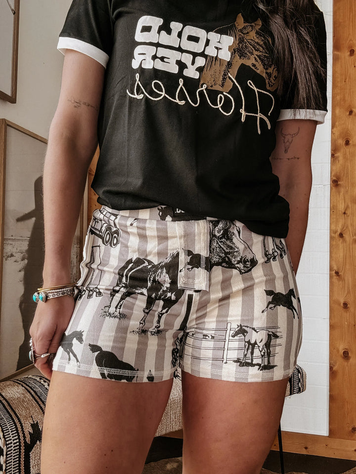 Person wearing a black t-shirt with graphic design and patterned shorts indoors.