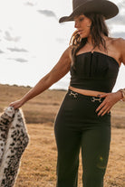 Woman in western black strapless top, high-waisted pants, and cowboy hat outdoors