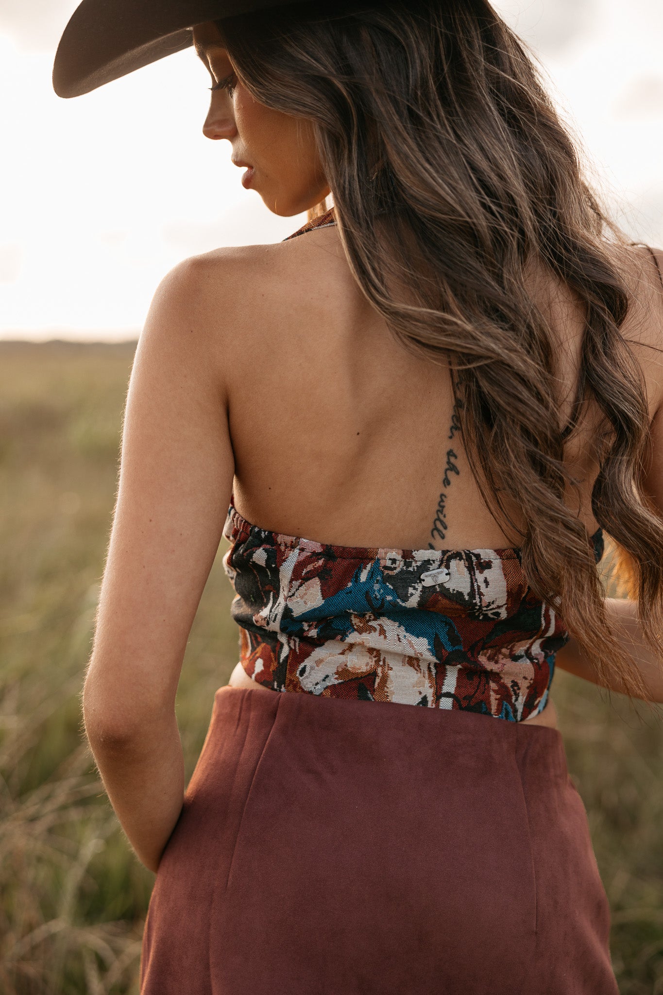 women wearing horse pattern halter top with low back and a Burgundy skirt standing in a field. 