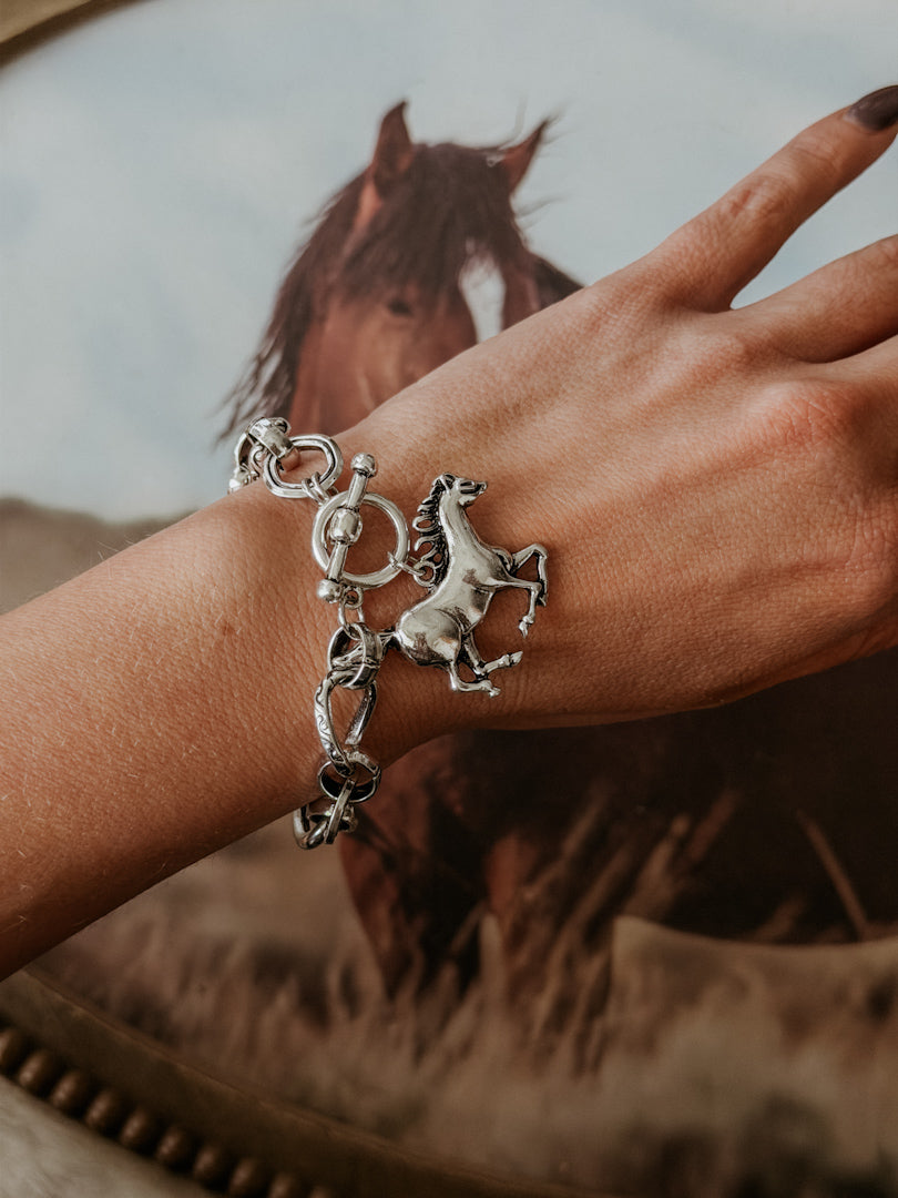 Western silver horse charm bracelet on woman's wrist, with horse art background.