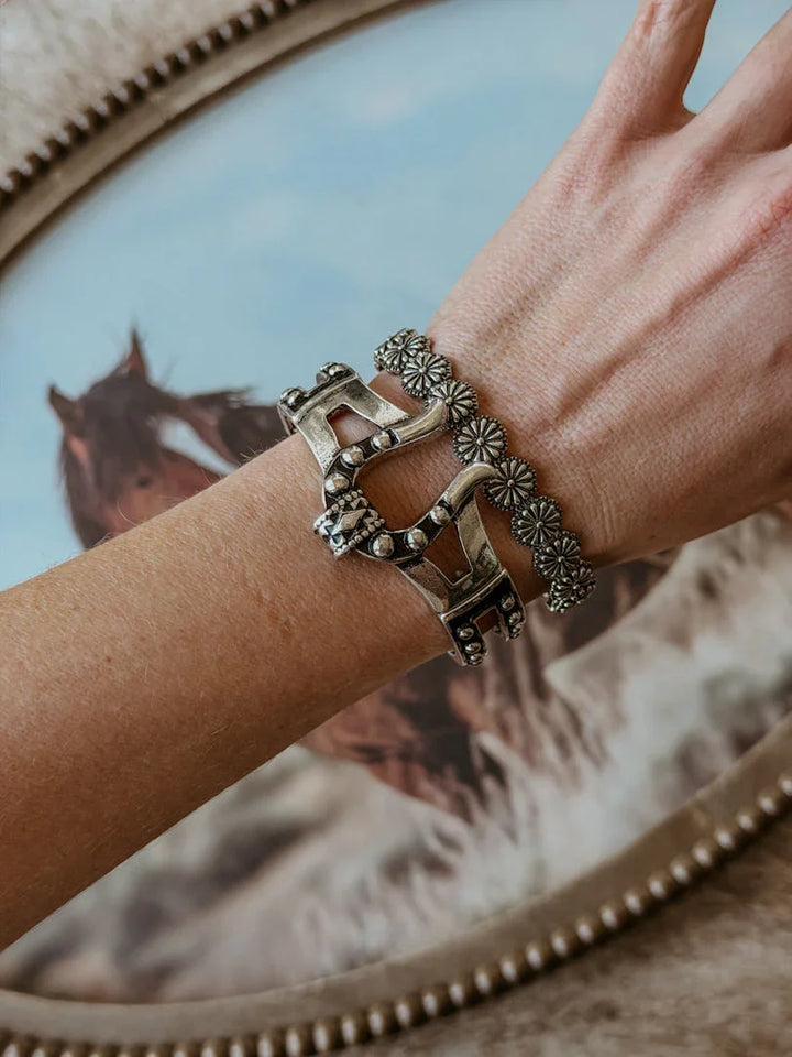 Silver western bracelet with horseshoe and floral designs on a wrist, horse art background