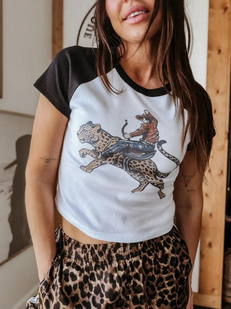 Woman wearing a white t-shirt with a graphic design and leopard print pants indoors.