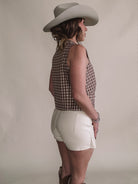 Woman in a western hat, checkered sleeveless top, white shorts, and cowgirl boots