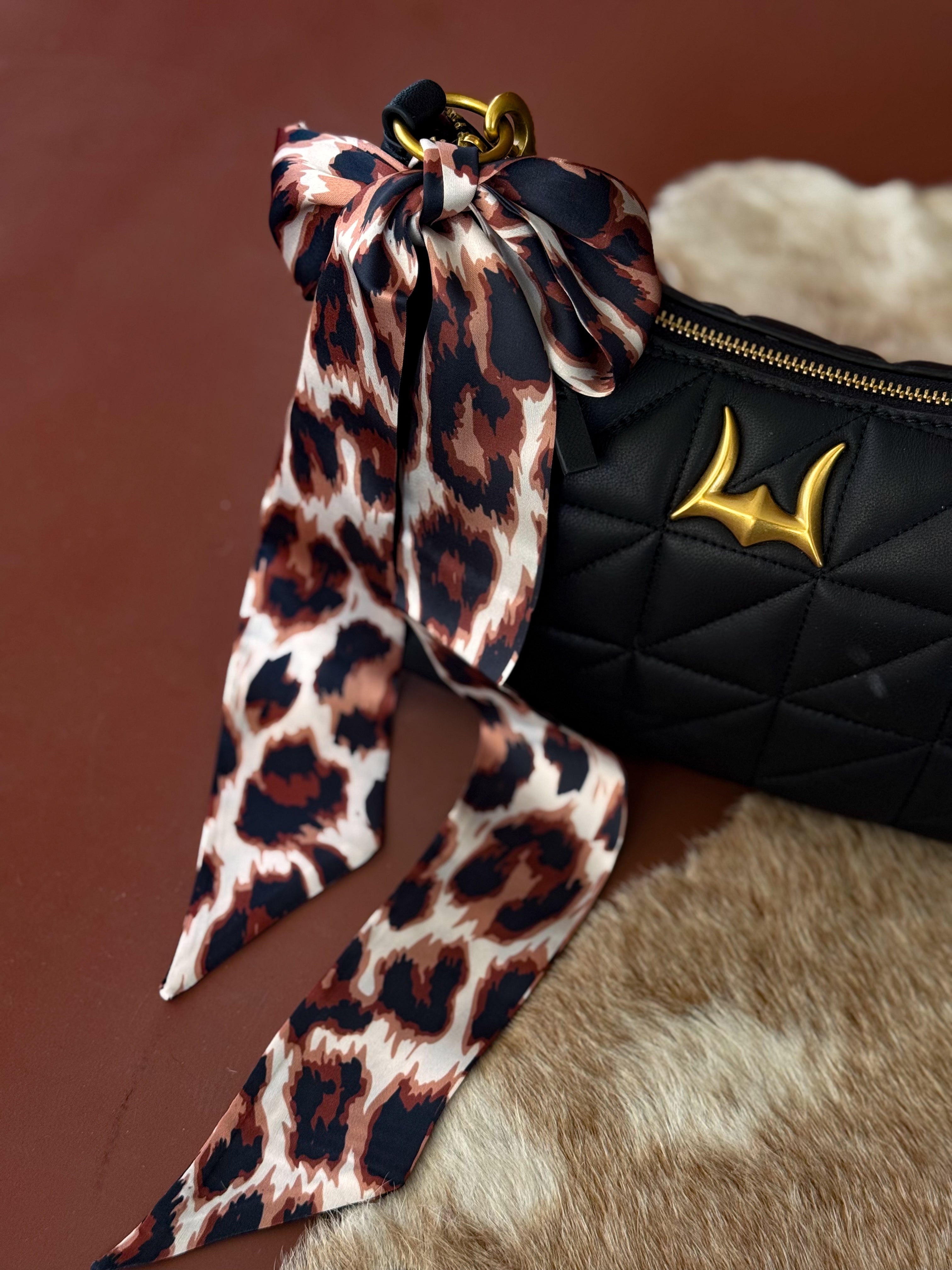 Quilted black western handbag with gold accent and leopard print bow on cowhide surface