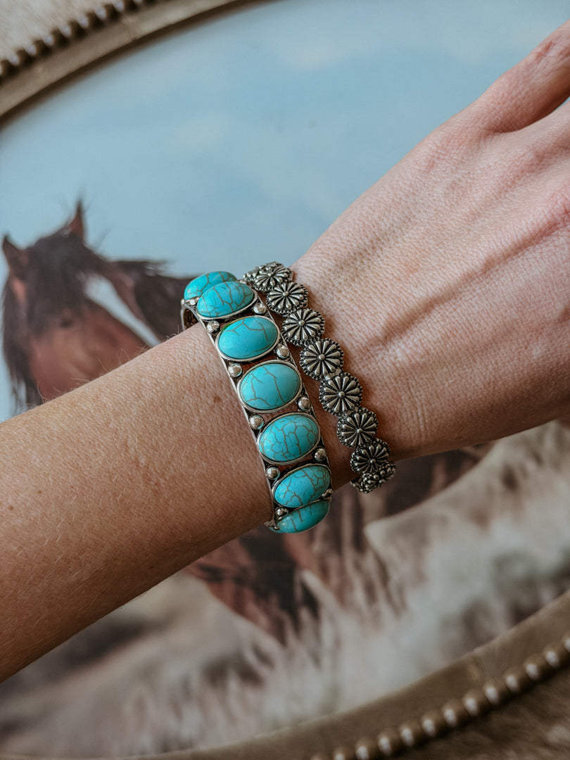Woman's wrist wearing western turquoise stone bracelet and silver concho bracelet, horse background