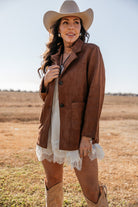 Woman in western suede jacket, cowboy hat, white lace dress, and cowboy boots outdoors