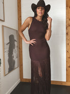 Woman wearing a dark brown dress with fringe and a cowboy hat indoors.