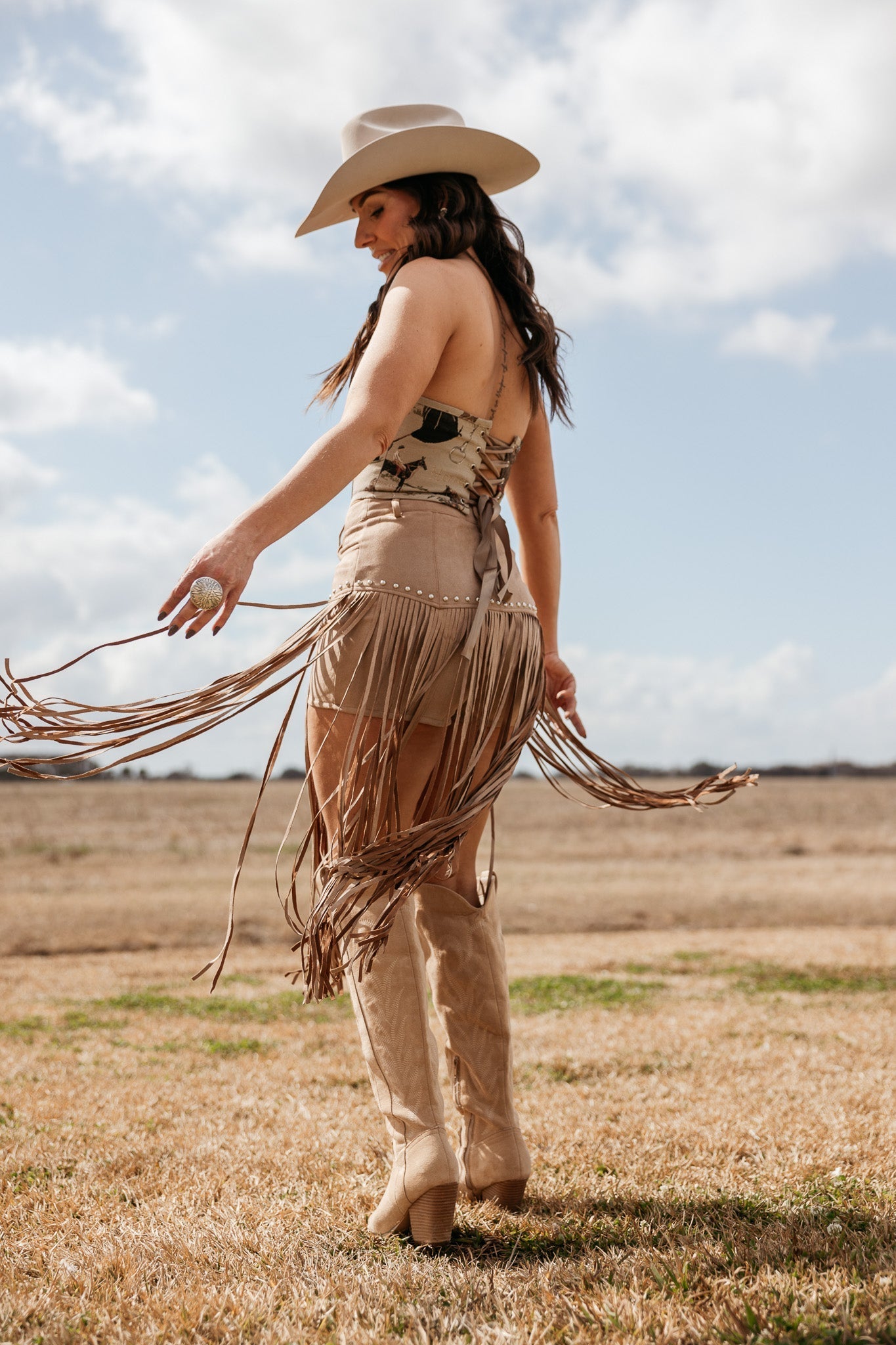 Woman in western boho outfit with fringe skirt, cowboy hat, and boots standing outdoors