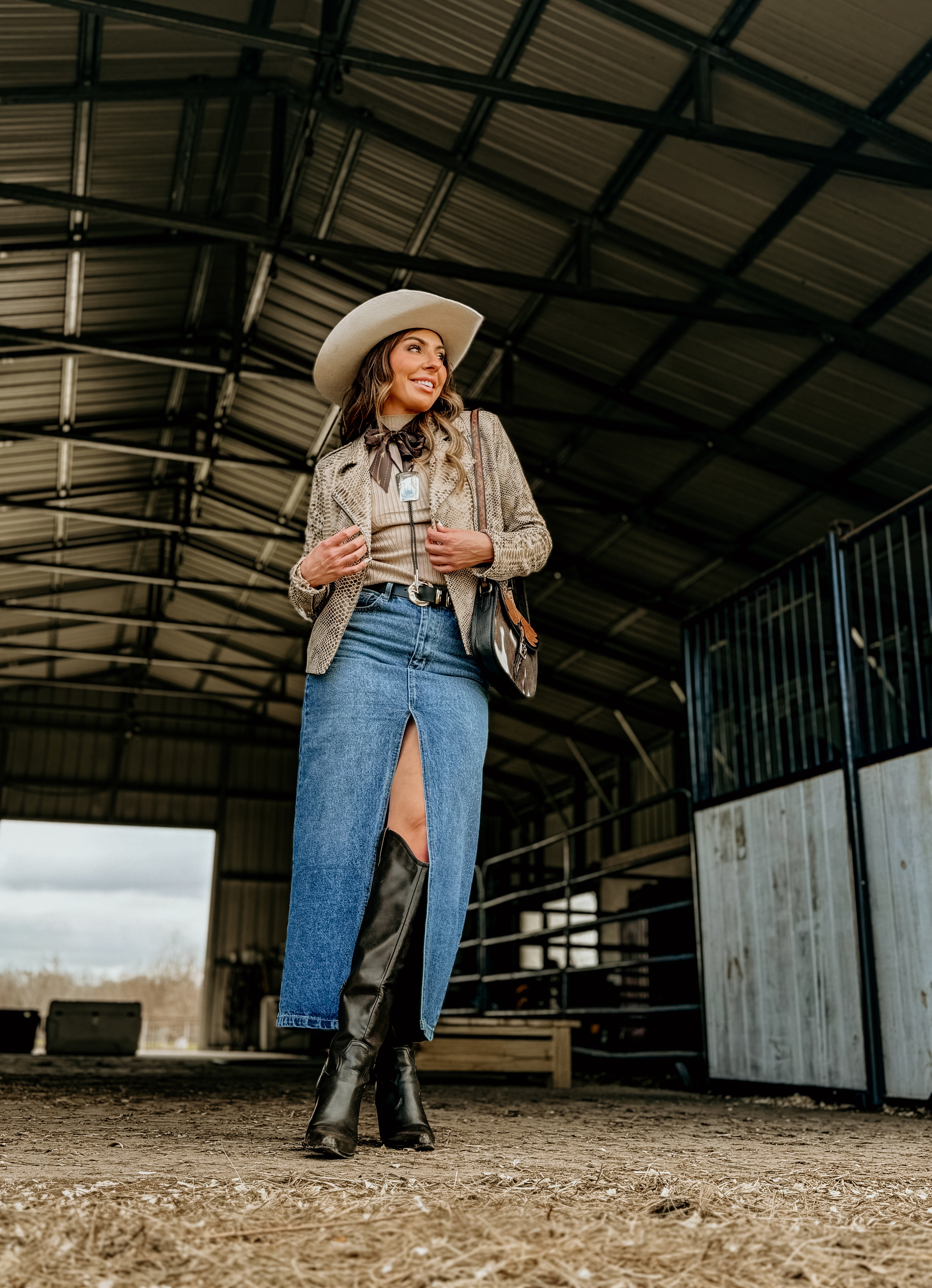 Woman in cowgirl hat, snakeskin jacket, denim skirt, and boots in a barn, western boho style