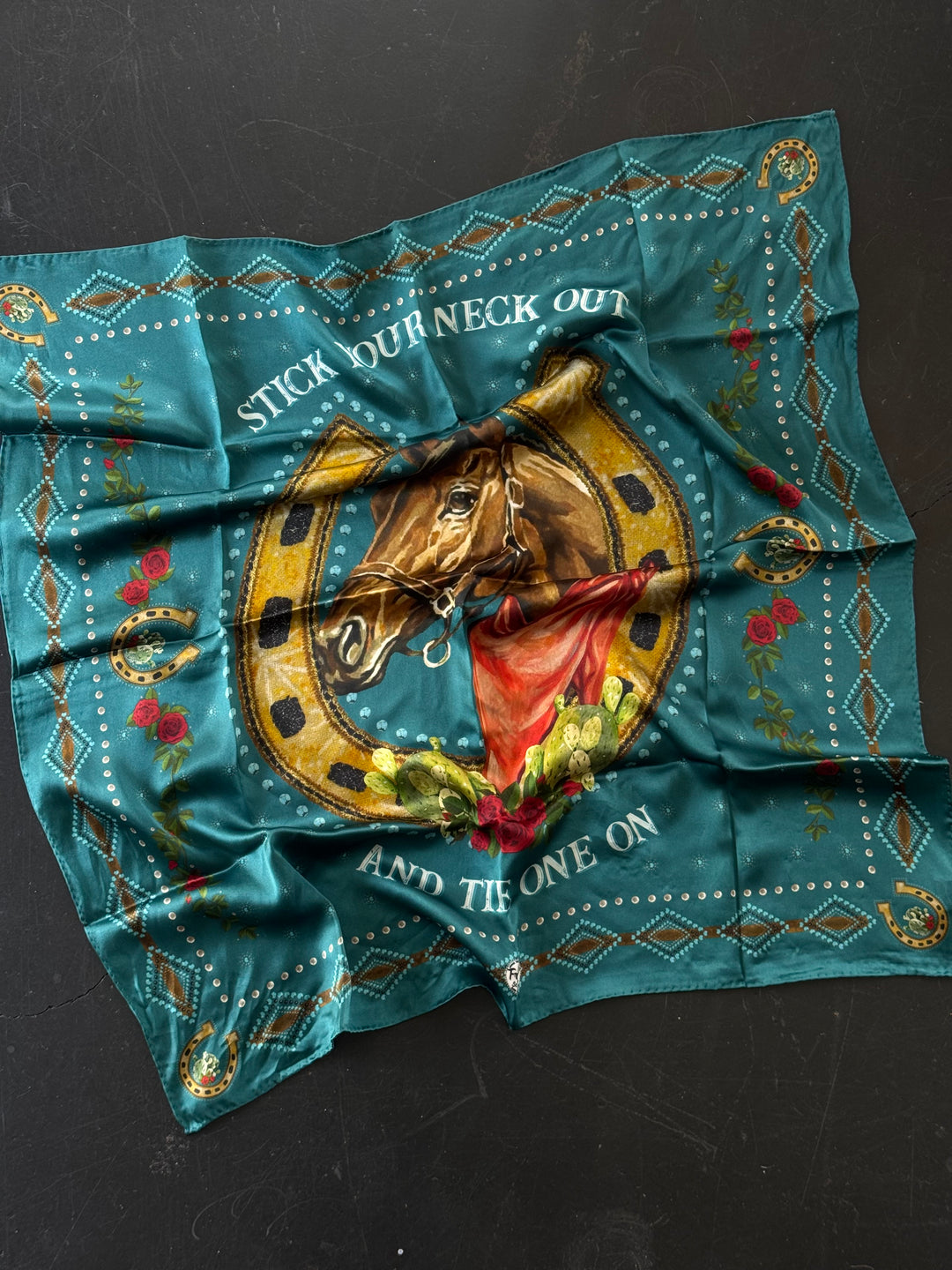Decorative teal scarf with horse and horseshoe design on a black background