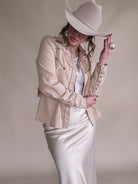 Woman in beige embroidered western shirt, satin skirt, and cowboy hat, showcasing boho cowgirl style.