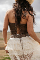 Woman in western boho outfit with lace skirt, brown corset top, wide belt, and cowboy hat