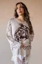 Woman in beige western knit sweater with brown cowboy hat pattern, layered over white lace skirt