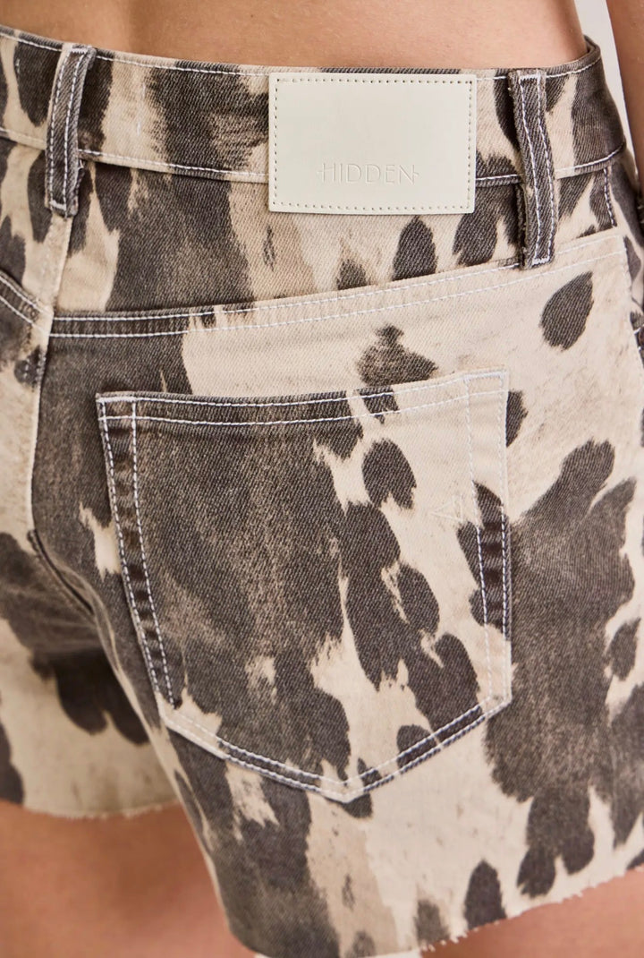 Close-up of a pair of shorts with a cow print pattern and a visible brand label.