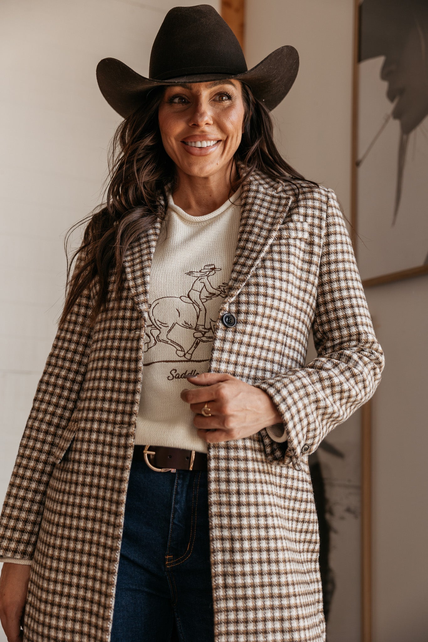 Woman in western boho outfit with plaid coat, cowboy hat, and graphic rodeo sweater