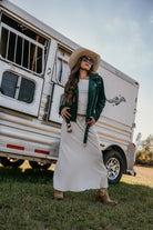 Woman in western boho outfit with suede jacket, maxi skirt, cowboy hat and boots by horse trailer