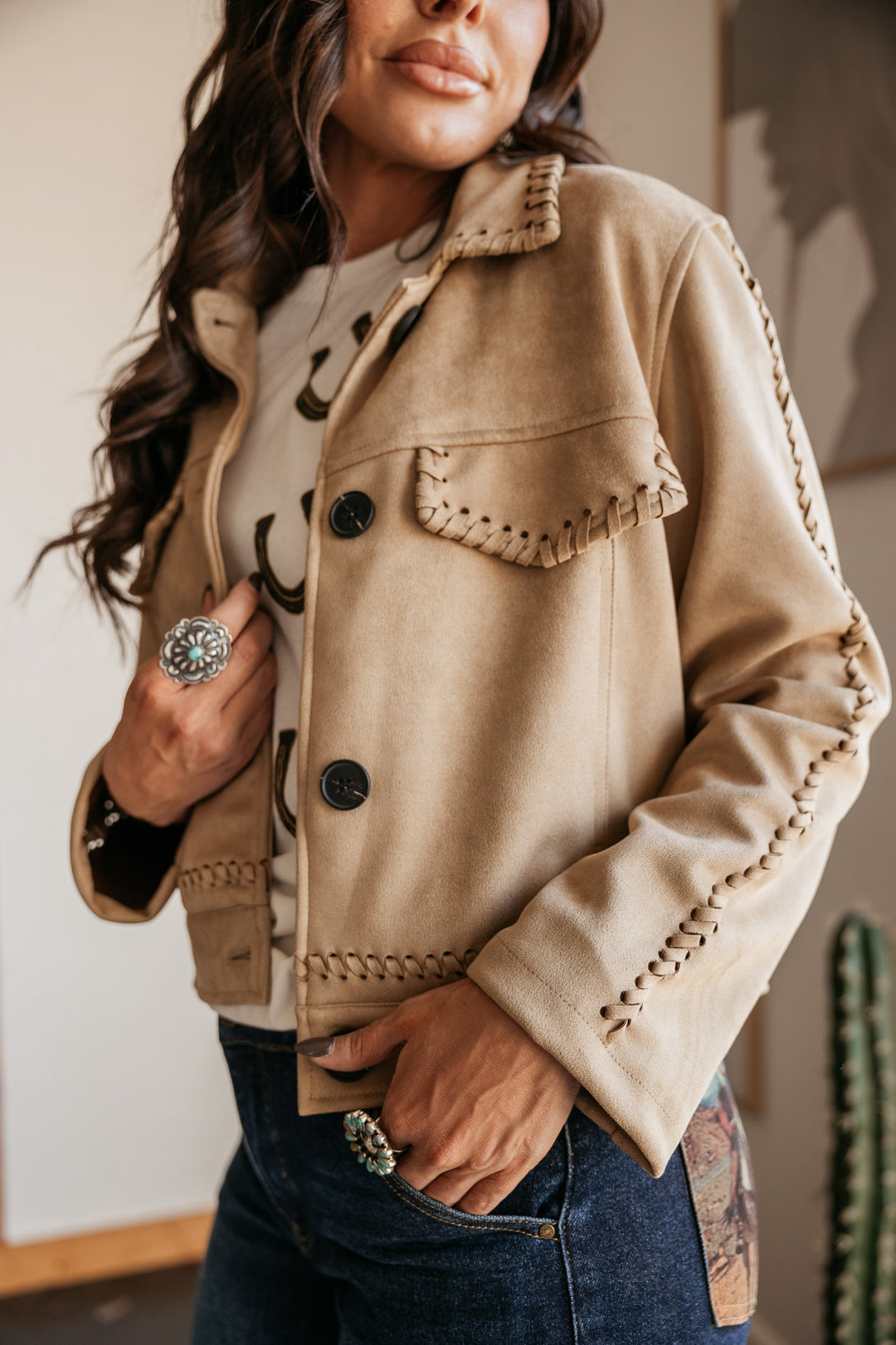 Woman wearing a beige jacket with decorative buttons and stitching.