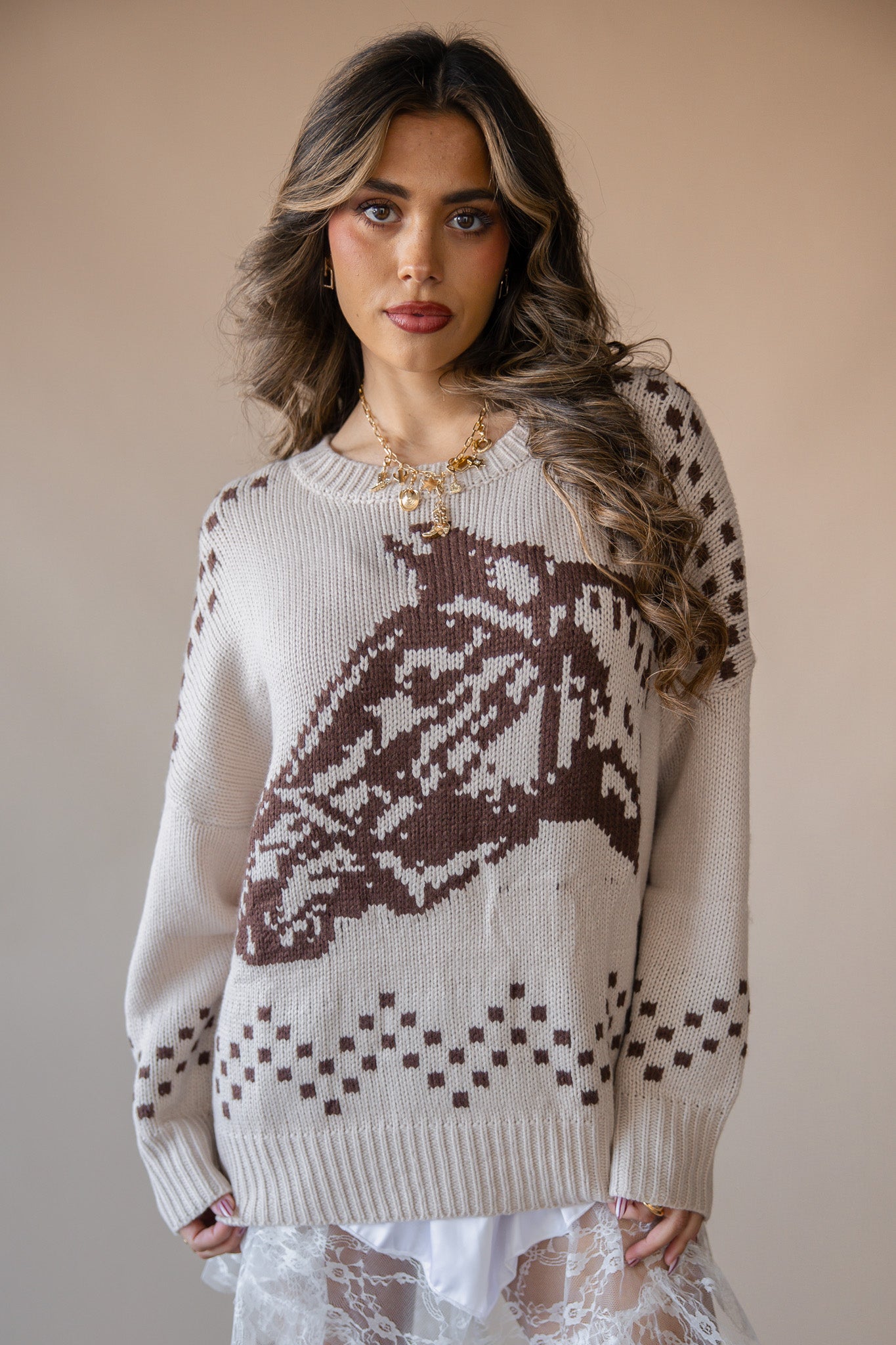 Woman wearing beige western sweater with brown horse pattern, lace skirt, and gold necklace