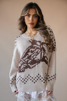 Woman wearing beige western sweater with brown horse pattern, lace skirt, and gold necklace