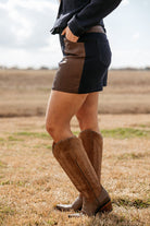 Woman in a western outfit with brown knee-high cowboy boots and brown patch shorts outdoors