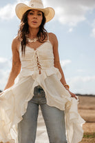 Woman in a white ruffled western dress, blue jeans, and cowgirl hat outdoors
