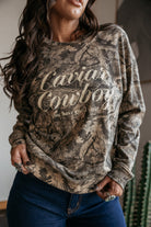 Woman wearing a western boho camo print "Caviar Cowboy" graphic sweatshirt and denim jeans