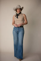 Woman in western outfit with wide brim hat, sleeveless top, flared jeans and neck scarf