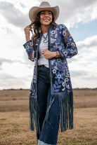 Woman in cowboy hat wearing sheer blue floral fringe duster, white top and jeans outdoors
