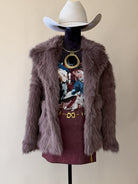 Mannequin wearing a fur coat, cowboy hat, and patterned top with a maroon skirt on a beige background