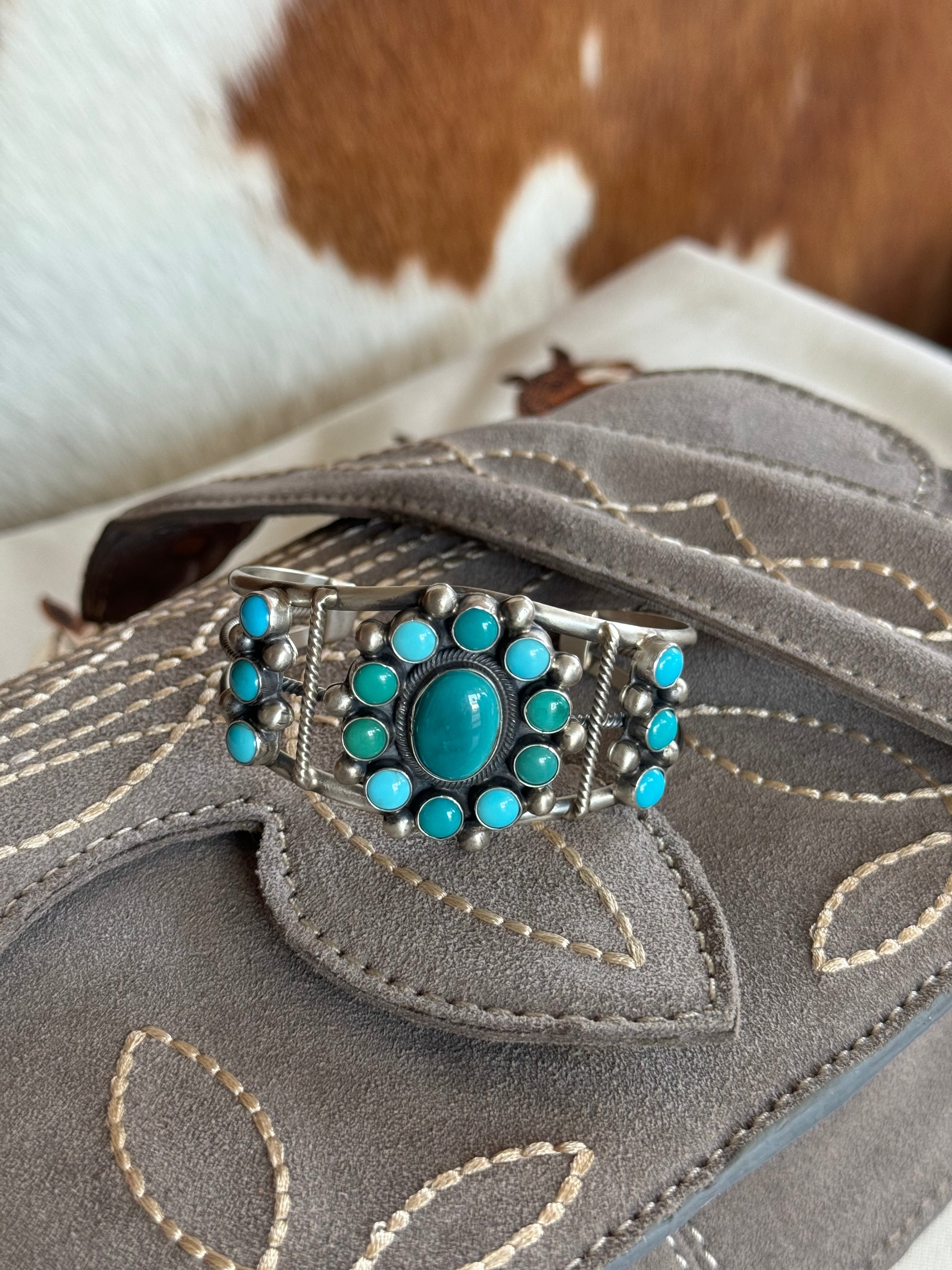 Turquoise and silver western cuff bracelet on embroidered grey suede purse, cowhide background