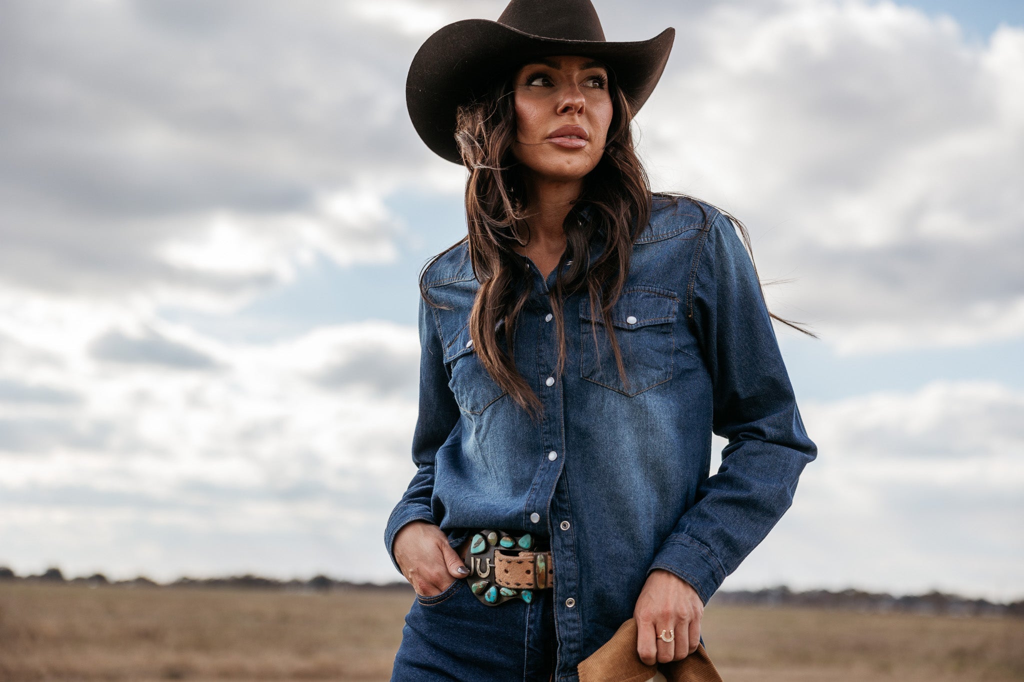 Woman in cowgirl hat and denim shirt with turquoise western belt outdoors